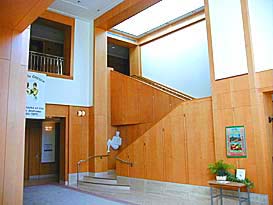 The lobby of the archives building has light colored wood walls, a staircase up to 2nd floor. In the corner a sculpture of woman
