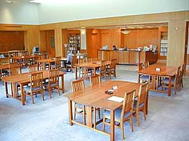 Several wooden tables and chairs fill the reference room.