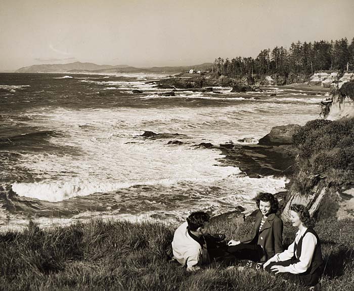 Three people relax on a grassy hillside over looking Boiler Bay.