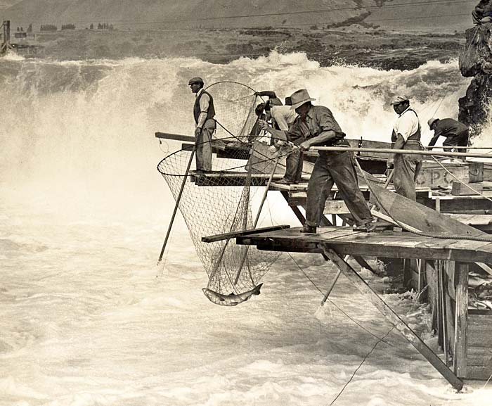 About half a dozen men on wooden shelfs stand with nets out over the falls.