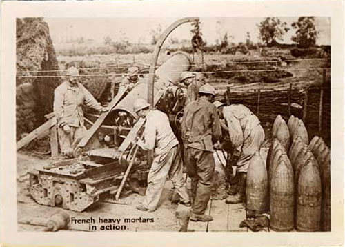 Four men operate a mortar piece with 3ft tall shells to the right.
