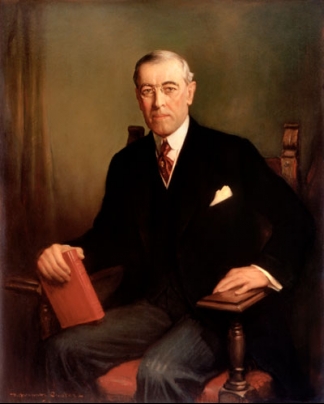 Woodrow Wilson sitting in a chair with a book in his hand.