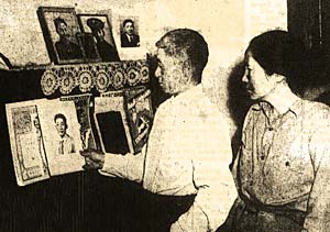 Japanese American man & woman look at photos on a wall in their home.