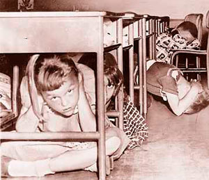 Photo of children crouching under their desks & covering heads with hands.