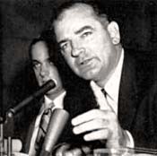 Photo of Senator McCarthy speaking into microphone. One hand is raised with a finger up like he's making a point.