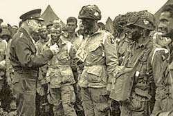Gen. Eisenhower talks with a group of dozens of soldiers in the field.