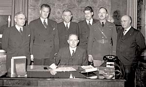 Seven men of the Oregon State Defense Council gather around a desk for a photo..