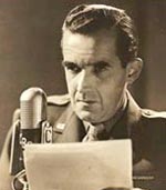 Edward Murrow sits in front of an old style radio microphone and holds a piece of paper in front of him.