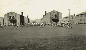 Barracks at Camp White near Medford in 1943 show men recreating outside in the dirt yard by large buildings.