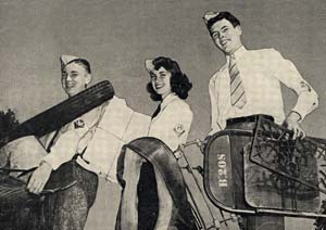 Photo of 3 teenagers (girl and 2 boys) carrying salvage material like metal chairs and newspapers.