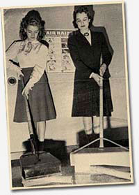 Photo of 2 women showing things that look like brooms or scoops with long handles.
