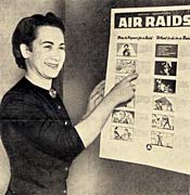 Woman smiles and points at an Air Raids poster on the wall.