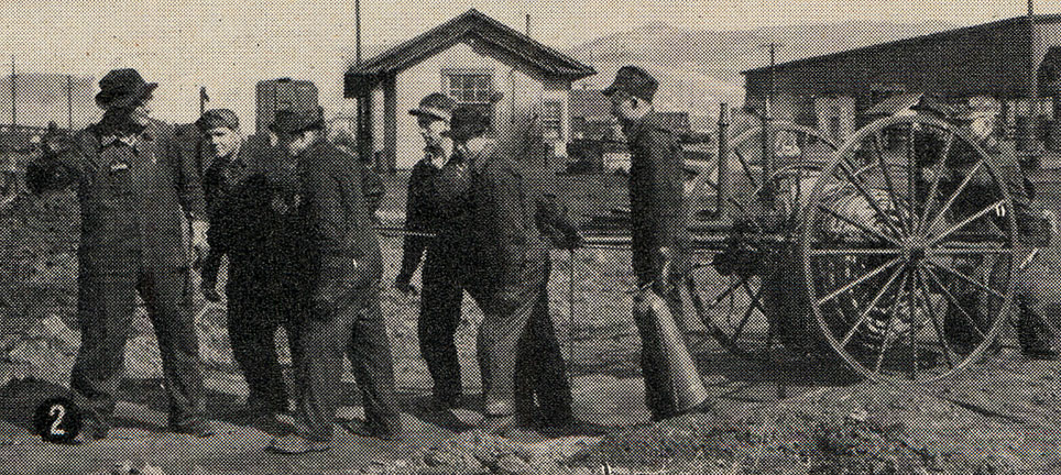 8 men in overalls and hats work with railroad equipment in a rail yard