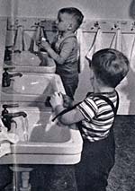 2 small boys at child size sinks in a bathroom wash their hands.