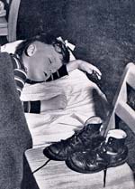 Photo of younb boy napping on a bed. His shoes are on a chair to the side.