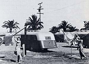 2 women hang up laundry outside a mobile home. There are palm trees in the background so the location probably isn't Oregon.