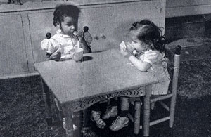 2 small girls sit at a child size table with cups of something.