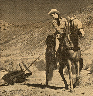 Photo of Roy Rogers on horse dragging scrap metal by a rope behind him.