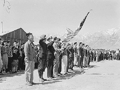 Japanese men and women lined up outside buildings with American flag.