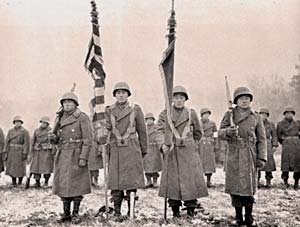 Men in military coats with helmets stand in lines. Front line holds flags. Looks like snow on ground.