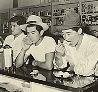Three Japanese men at a counter in a drug store eating & drinking.