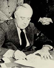 Rossevelt sitting at a desk signing a piece of paper.