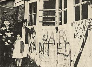 Mother, father, 2 small children stand in front of hate messages spray painted on their home.