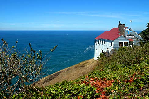 Red roofed cottage on a cliff looks out over blue ocean and clear sky.