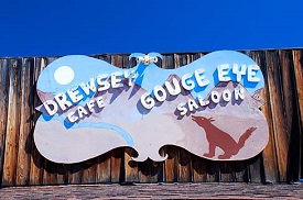 Sign has drawing of dog & sand dunes with name of cafe & saloon above.
