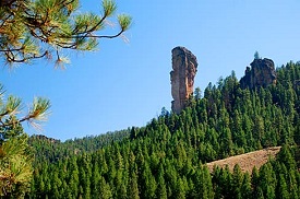 A tall and thin rock formation juts up above a forested landscape.