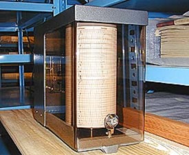 A chart on a circular tumbler encased in glass and set on a wooden table. A temperature gauge is attached to the front.