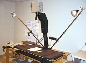 Camera mounted about 4 feet above a table with lights on movable arms to the side.