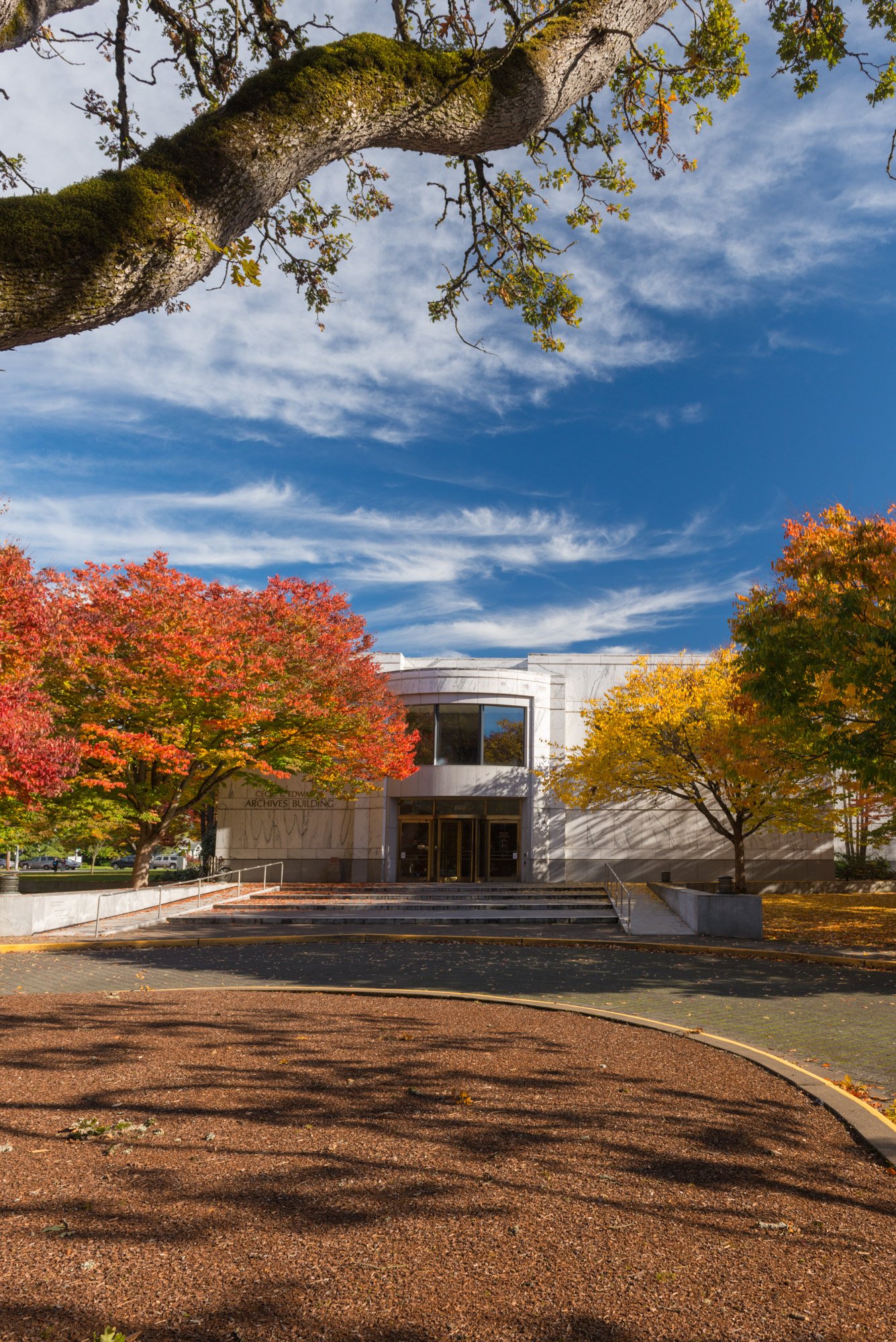 Exterior view of the Oregon State Archives building on a clear day, showing its modern architecture with large windows and a landscaped walkway in front.