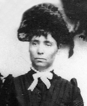 Photo of Susan Mathews in black dress and hat with white bow tie around neck.