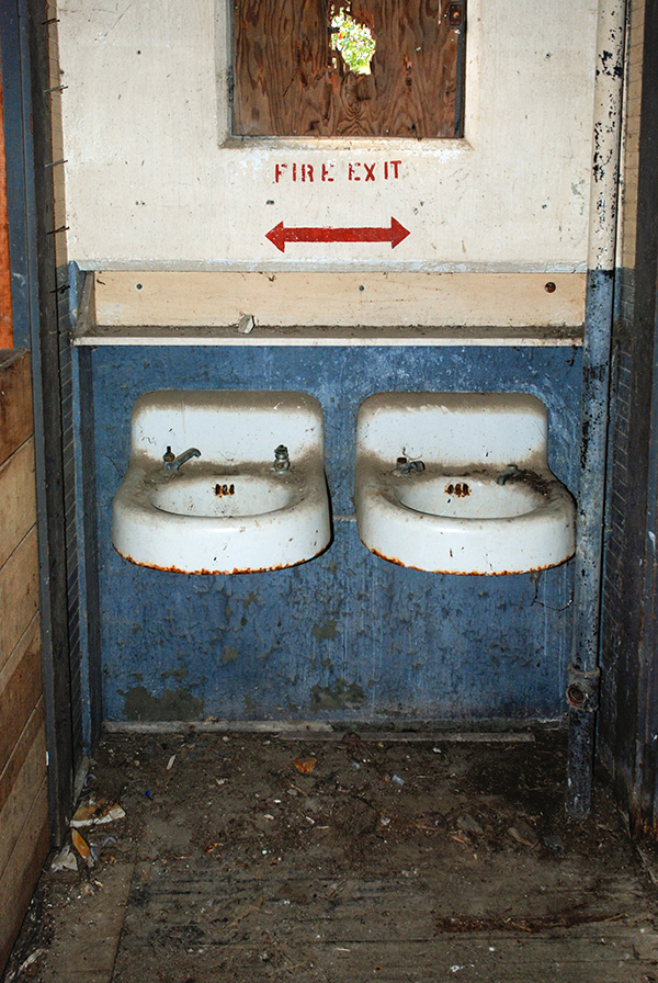 Two rusted, dirty sinks attached to a wall. 