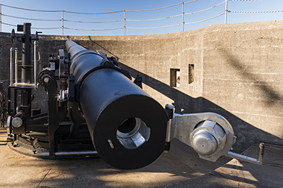 View of a cannon from the backside with the shute open where the ammunition is loaded. It is set in a sunken area of stone.