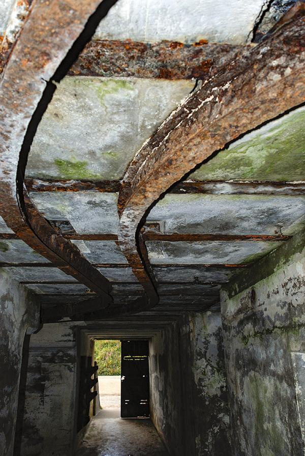 Two rusted metal rails run in a curved manner along the ceiling of a stone room. 