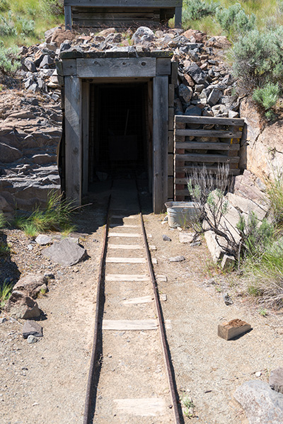 Opening framed in wood beams leads into dark hole. An old rail track leads into the opening.