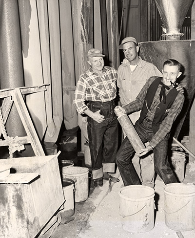 2 men smile and stand next to another man (Algot Sunderlin) who's holding a 2 ft long cylinder.