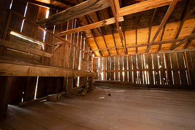 Inside a wood plank building the sunshine is visible through the space between each slat. Wood plank floor and ceiling.