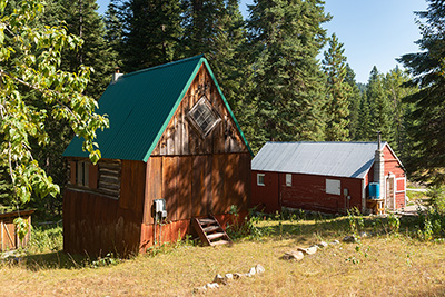Two wood frame homes with metal roofs. Tall evergreen trees surround the area.