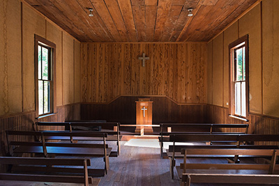 Inside the church are wood pews facing a podium with a cross. Wainscotting on walls and wood siding & ceiling.