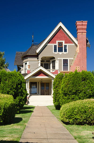 Queen Anne style house built in 1892. A brick chimney runs up the right side & hedges line the front walk.
