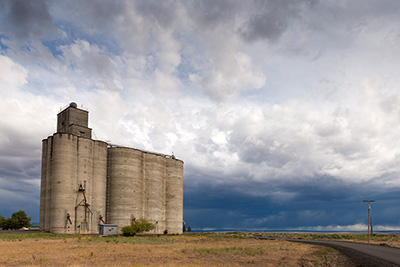 A grain elevator next to a paved road. Storm clouds in the sky.