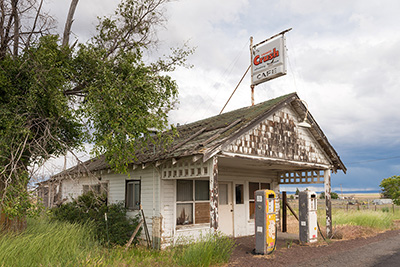 Old building with pealing paint and rotted roof. An "Orange Crush" drink sign hangs on the roof.