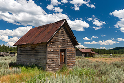 A one-room, one-story wood plank building in a field. The wood is pealing and weather worn.