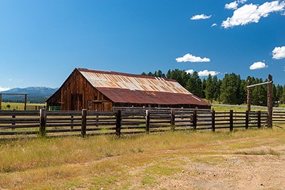 A wood barn with a metal roof in a field surrounded by a wooden fence. 