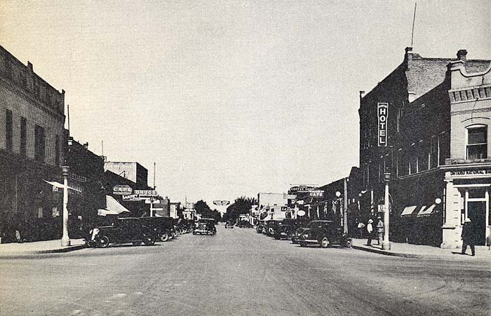 Downtown Ontario street, 1940, cars lining parking spots on street and businesses on each side. A hotel sign shows on right