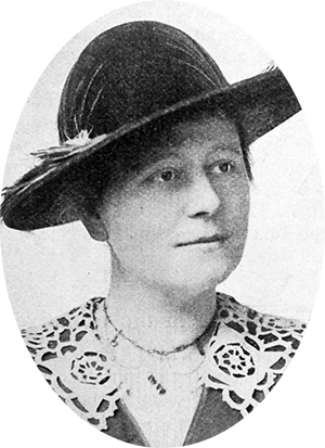 Photo of Kathryn Clarke wearing a brimmed hat & a lace collar over her dress.