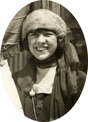 Photo of a young Betty Gram, smiling at the camera & squinting in the sunshine of outdoors.